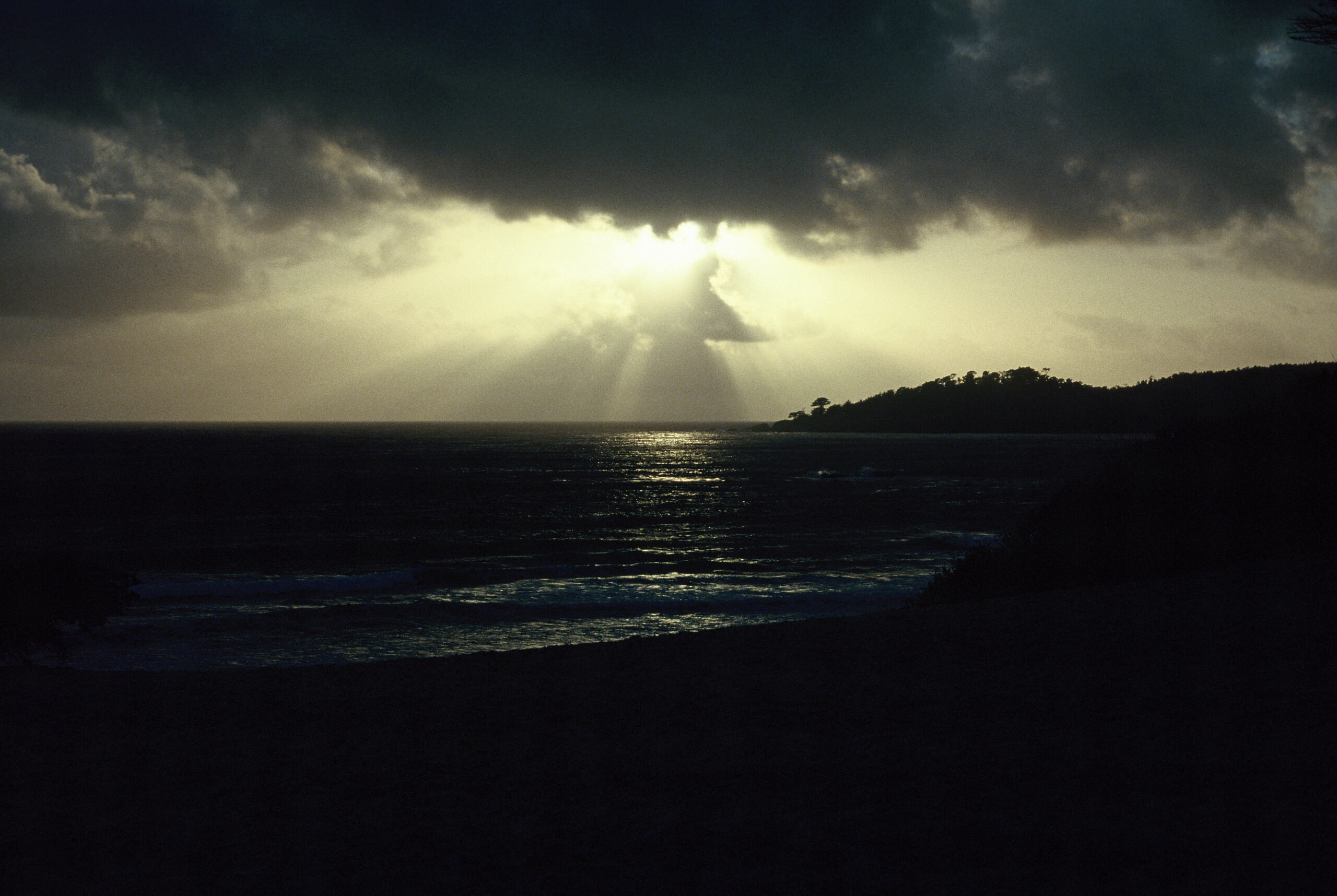 A break in a dark cloud bank over the Pacific, sunlight streaming down through the gap, the cloud within the light resembling a robed figure with arms outstretched.